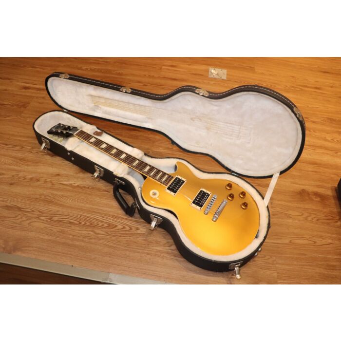 Esta guitarra Gibson Slash Signature Gold Top é um modelo usado, mas ainda em ótimo estado. Com um acabamento dourado brilhante e o icônico logotipo  polSlash pol na cabeça, esta guitarra é uma homenagem ao lendário guitarrista do Guns N' Roses. Possui ca